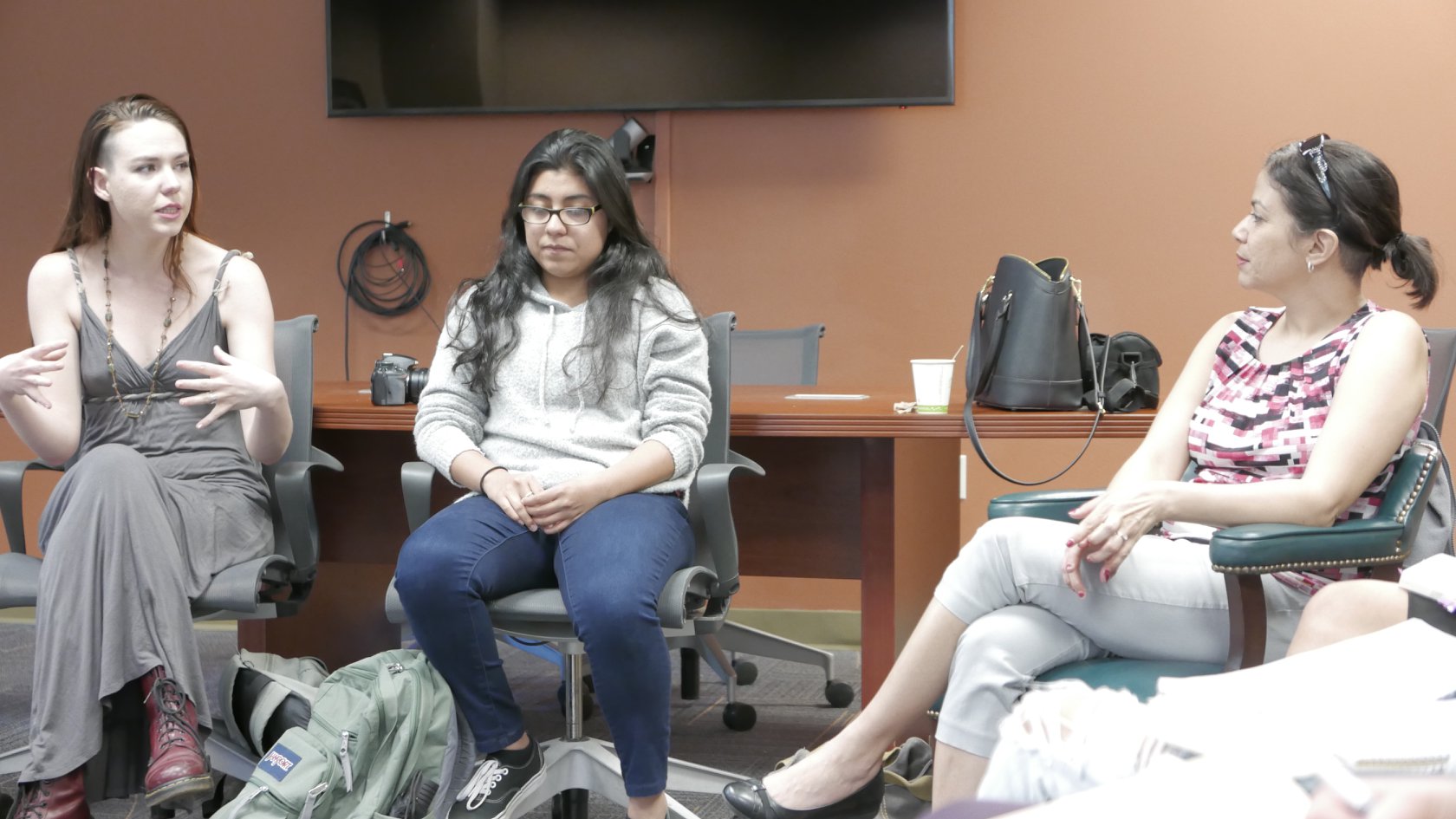 Two students, one of whom is speaking and gesturing animatedly, sitting to the left of Daisy Hernández in a large conference room.