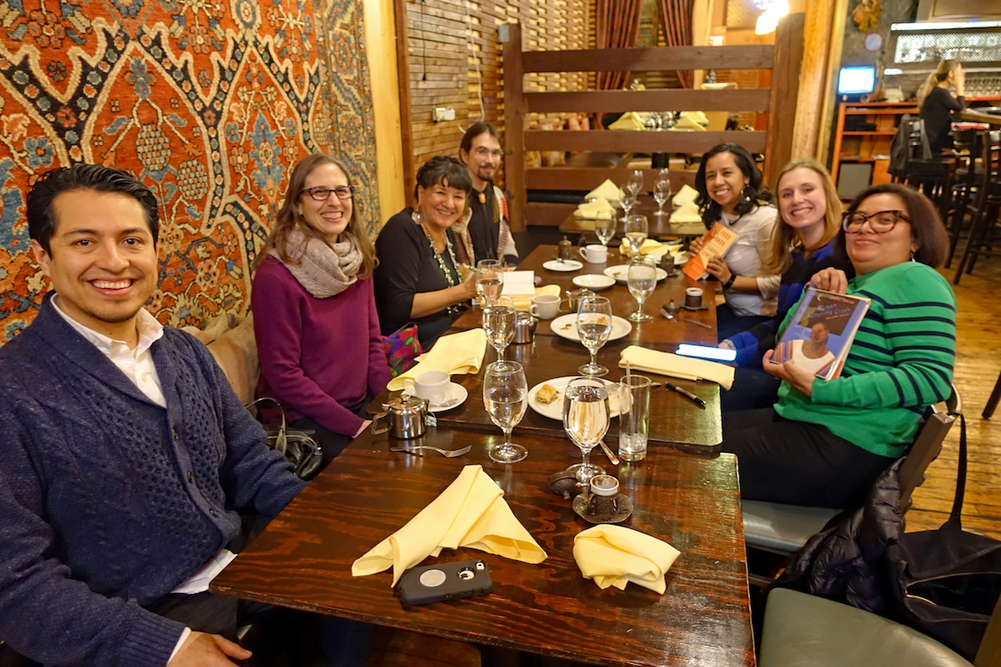 A small group of students and faculty posing for a photo with Sandra Cisneros as they sit around the table at a post-event dinner.